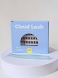 Cloud Lash false eyelash kit with a light blue box, a pair of matching light blue tweezers, and a window showing the lashes inside, displayed on a white round pedestal against a light beige background.