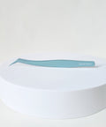 A pair of light blue curved tweezers with the brand name 'Cloud Lash' printed on the handle, resting on a white cylindrical pedestal against a light gray background.